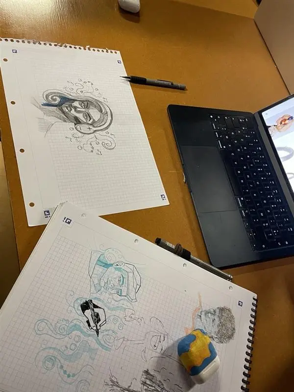 Croquis artistiques sur papier représentant des visages stylisés en formes géométriques, posés à côté d'un ordinateur portable.